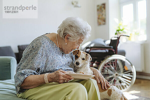 Glückliche ältere Frau hält einen Teller mit Essen in der Hand und streichelt den Hund zu Hause