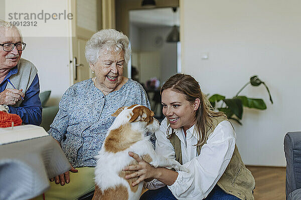 Happy senior couple with healthcare worker stroking dog at home