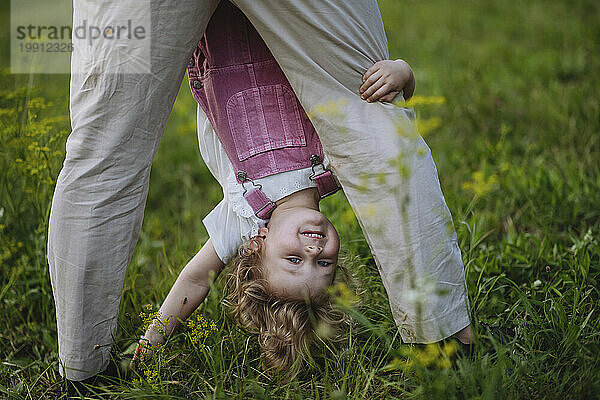 Little girl looking through father's legs holding her upside down