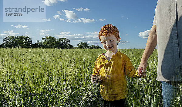 Smiling boy holding hand of grandmother walking in field