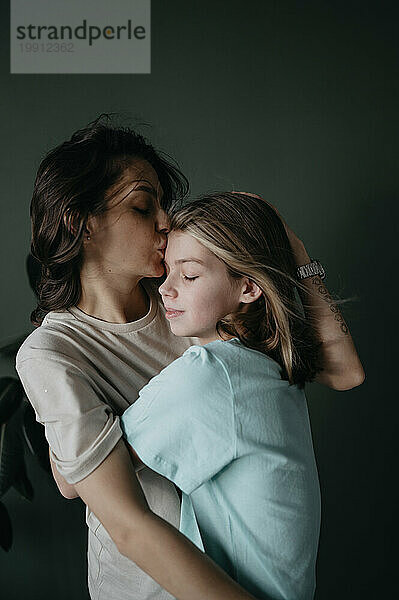 Liebevolle Mutter umarmt und küsst ihre Tochter zu Hause auf die Stirn