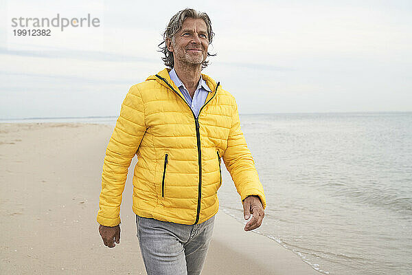 Lächelnder Mann mit gelber Jacke und Spaziergang am Strand
