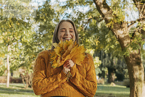 Glückliche Frau hält einen Haufen Ahornblätter im Herbstpark