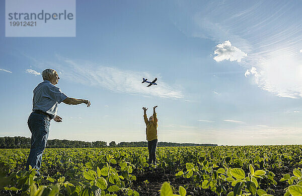 Grandfather flying toy airplane with grandson enjoying in field