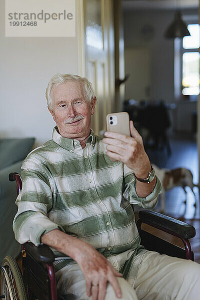 Lächelnder älterer Mann  der zu Hause ein Selfie mit dem Smartphone macht