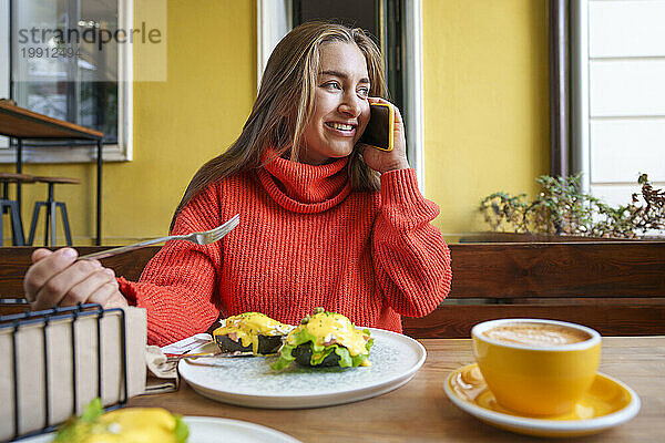 Lächelnde Frau sitzt im Straßencafé und telefoniert mit ihrem Smartphone