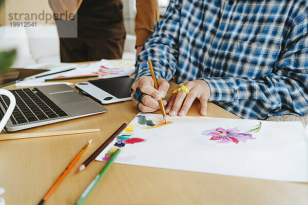Young graphic designer coloring on paper at desk in office