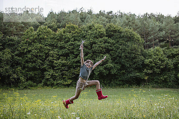 Mädchen springt in der Natur und hält ein Modell einer Windkraftanlage in der Hand