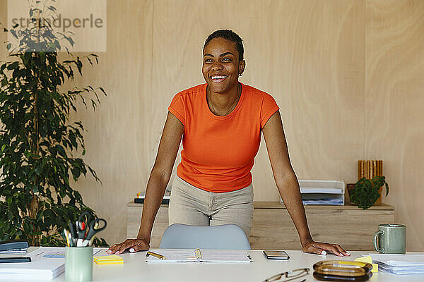 Glückliche Geschäftsfrau lehnt am Schreibtisch im modernen Heimbüro