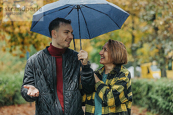 Glückliche Mutter mit Sohn  der Regenschirm hält und im Herbstpark redet