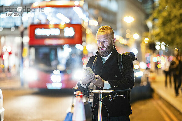 Reifer Mann surft nachts mit Smartphone in der Stadt im Internet