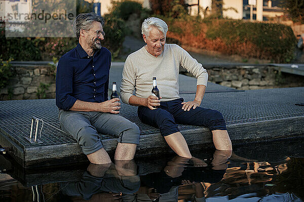 Happy senior friends sitting on pier with beer bottles