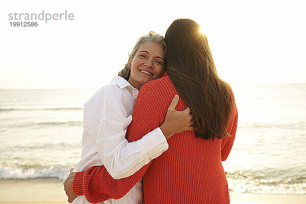 Glückliche Mutter umarmt Tochter am Strand