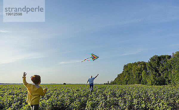 Grandfather and grandson flying kite in agricultural field under sky