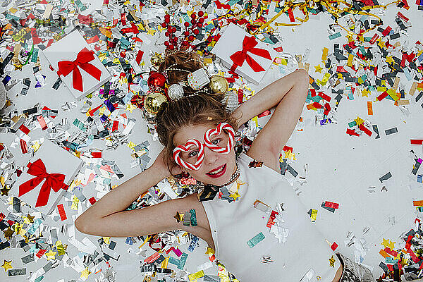 Lächelndes Mädchen liegt auf Konfetti neben Weihnachtsgeschenken