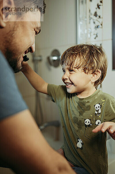 Playful boy brushing teeth of father in bathroom at home
