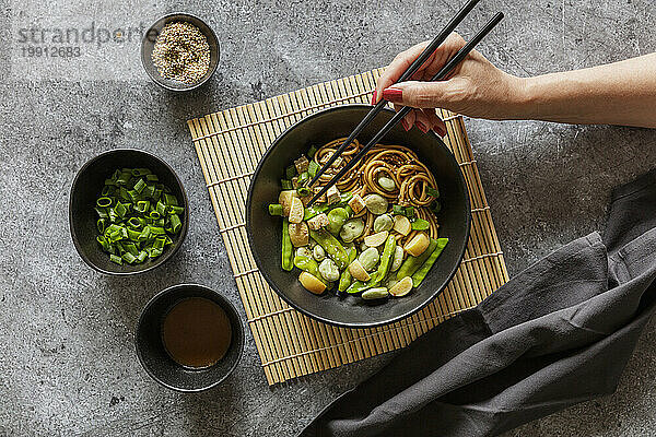Hand of woman eating bowl of vegan miso udon bowl with tofu  snap peas  broad beans and turnips