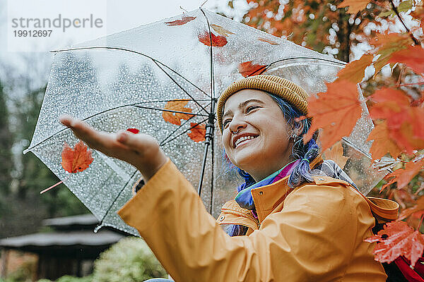 Lächelnde Frau hält Regenschirm und genießt Regen im Herbstpark