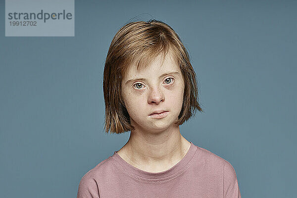 Trauriges Mädchen mit Down-Syndrom vor blauem Hintergrund