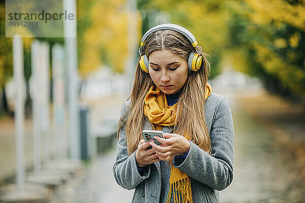 Frau mit kabellosen Kopfhörern benutzt Smartphone auf der Straße