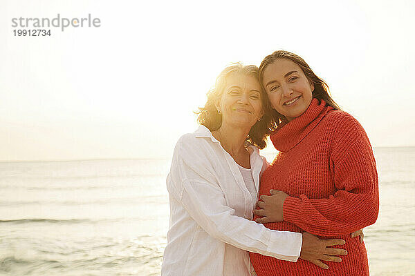 Lächelnde Mutter und Tochter stehen zusammen am Strand