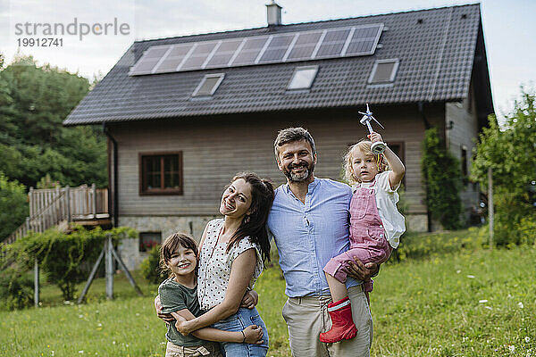 Junge Familie vergnügt sich vor ihrem Einfamilienhaus mit Sonnenkollektoren auf dem Dach