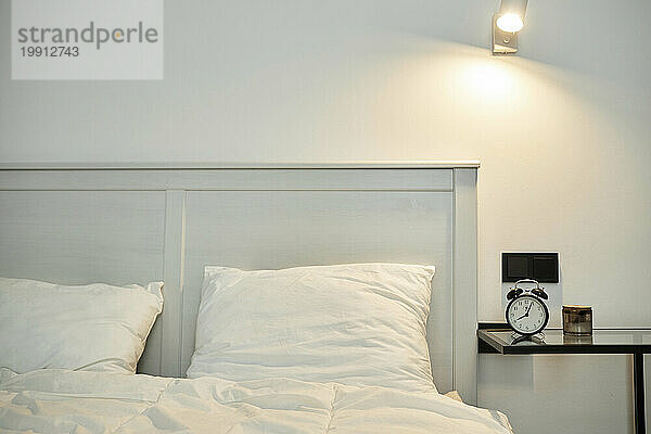 Bedroom interior  bed with white linen and bedside table with alarm clock on it