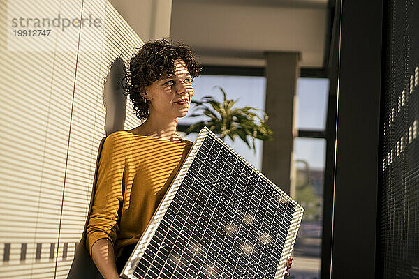 Lächelnde Geschäftsfrau hält Solarpanel im Büro