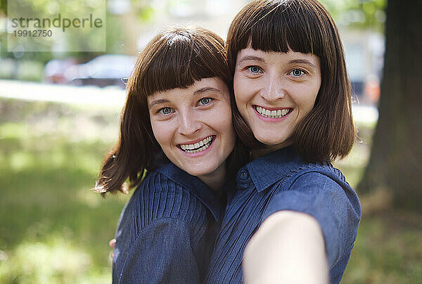 Lächelnde Zwillingsschwestern machen Selfie im Park