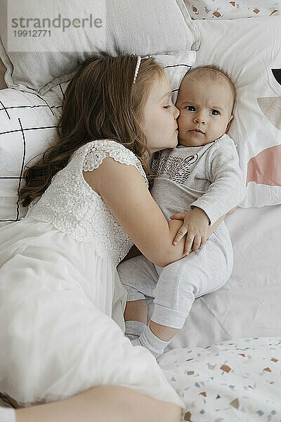 Loving sister embracing and kissing brother's cheek on bed