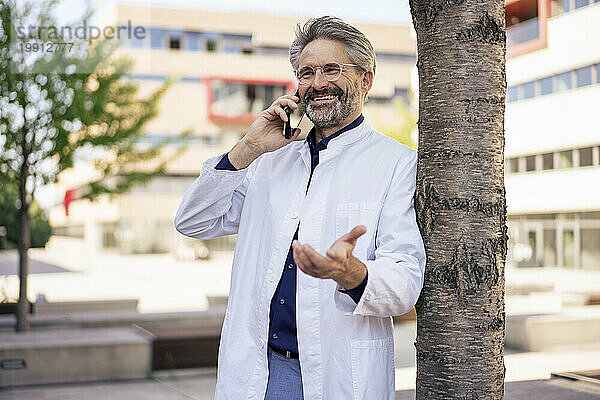 Fröhlicher Arzt  der mit dem Handy gestikuliert und spricht