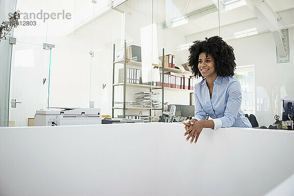 Smiling young businesswoman leaning at office