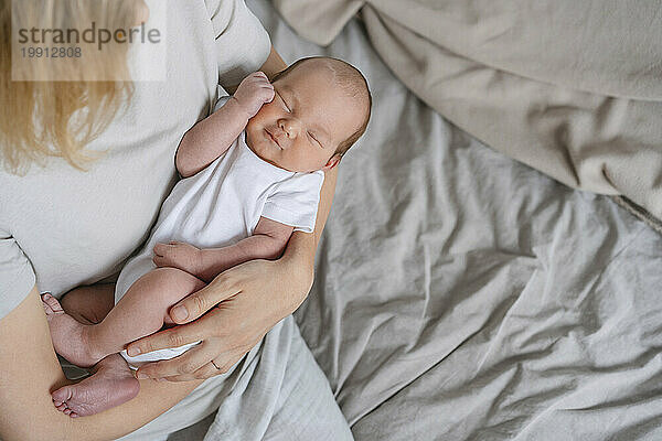 Newborn baby boy sleeping in arms of mother at home