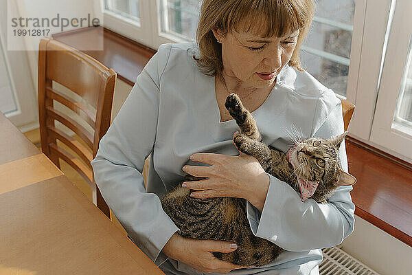 Ältere Frau umarmt Katze zu Hause im Arm