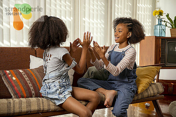 Happy girls playing clapping game on sofa at home