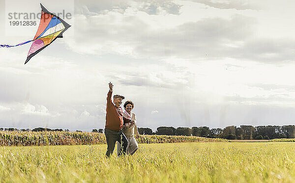 Happy senior couple flying kite in field on sunny day
