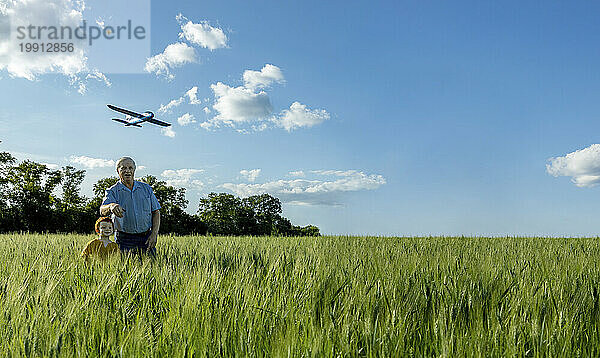 Grandfather and grandson playing with toy airplane in field