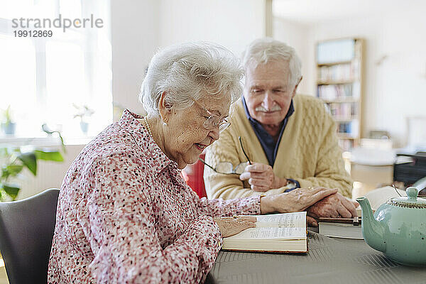 Älterer Mann und Frau lesen Buch und halten Händchen am Tisch