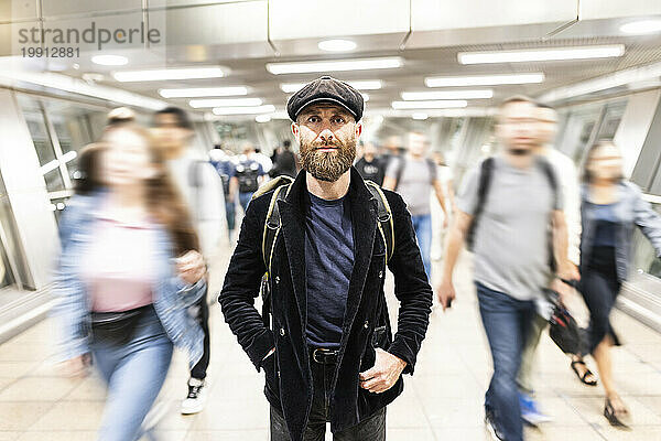 Reifer Mann steht inmitten von Menschen  die sich an der U-Bahn-Station bewegen
