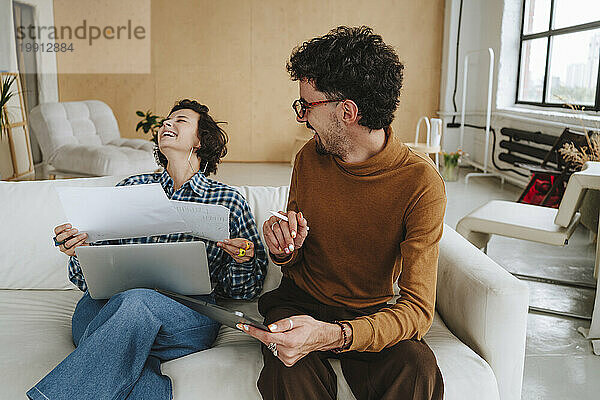 Glücklicher Grafikdesigner sitzt mit Kollege lachend auf dem Sofa im Büro