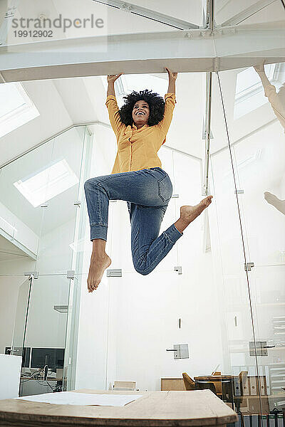 Playful businesswoman hanging on iron bar at office
