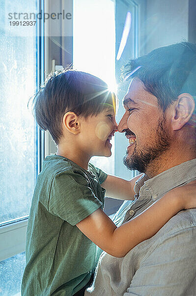 Liebevoller Vater und Sohn reiben sich zu Hause am Fenster die Nase