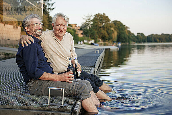 Glücklicher älterer Mann  der mit einem Freund am Steg Bier genießt