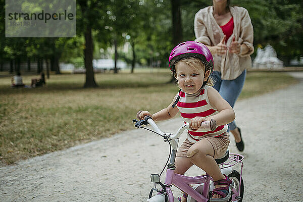 Kleines Mädchen lernt im Stadtpark Fahrradfahren mit Fahrradhelm