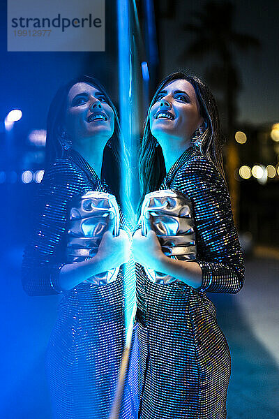 Lächelnde Frau lehnt an einer Glaswand mit Neonbeleuchtung