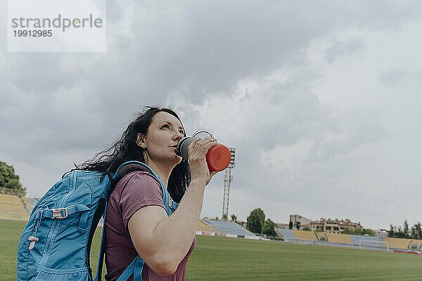 Frau trinkt Wasser aus einer Flasche unter dem Himmel