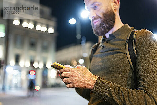 Reifer Mann mit Bart  der nachts in der Stadt sein Mobiltelefon benutzt