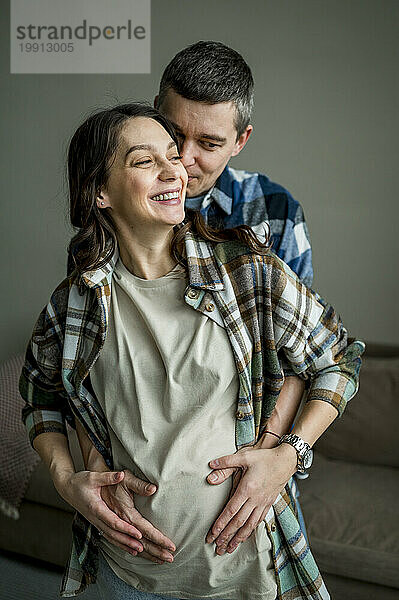 Liebevoller Mann hält zu Hause die Hände einer schwangeren Frau auf dem Bauch