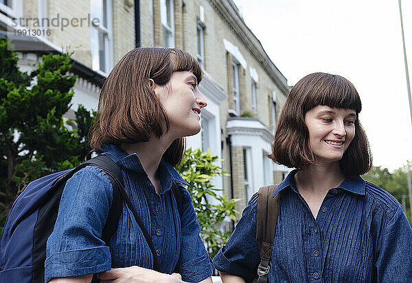 Glückliche Zwillingsschwestern mit Rucksäcken vor dem Gebäude