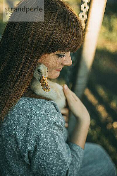 Young redhead woman with freckles holding duckling